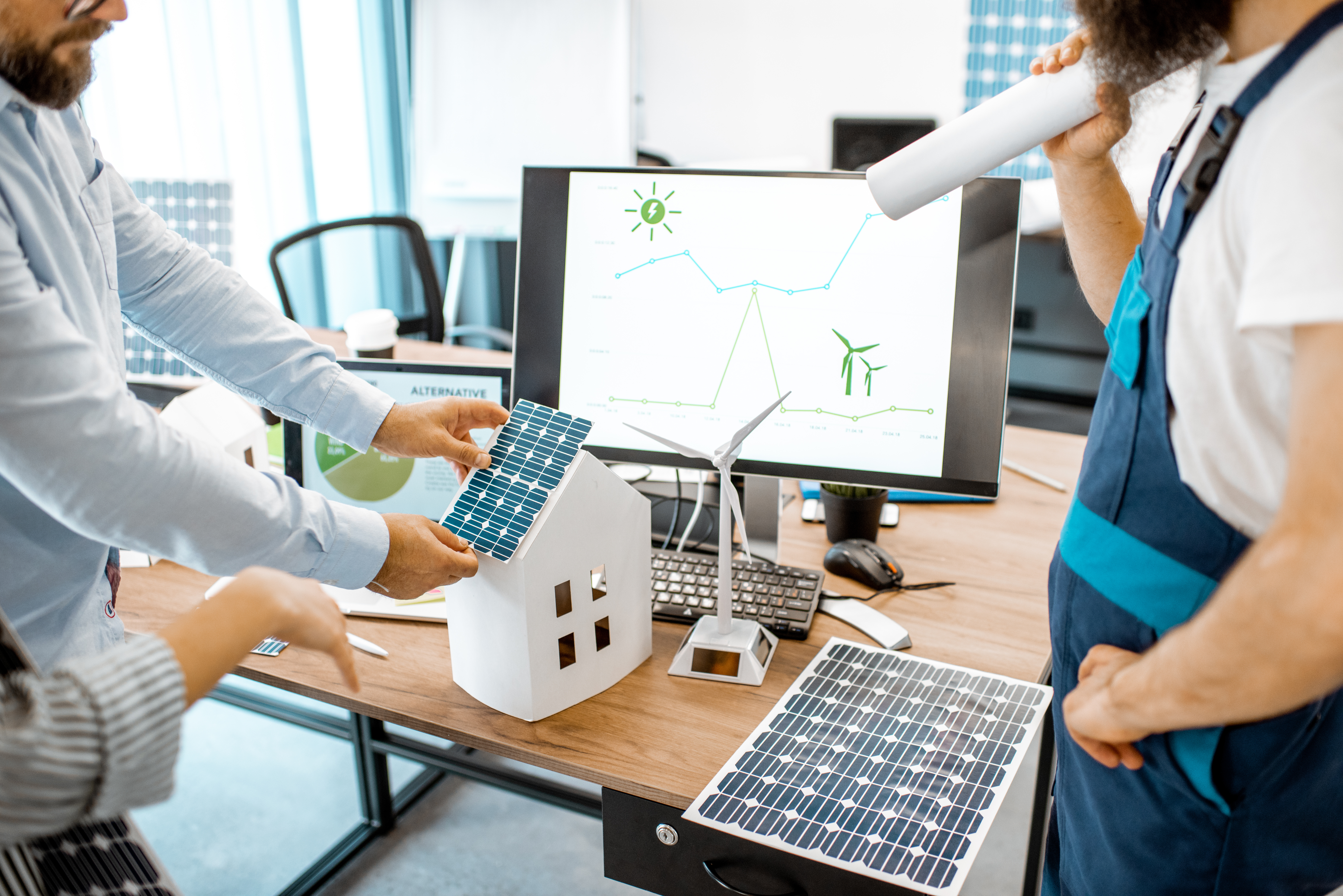People working on a project of alternative energy, working with house model and computer in the office, close-up on the working place